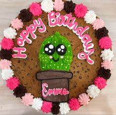 a decorated birthday cake with a cactus and name written on the frosting, surrounded by flowers