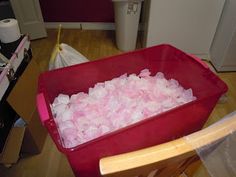 a red container filled with ice cubes sitting on top of a wooden floor next to a trash can