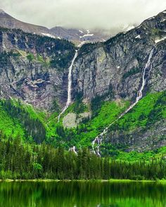 the mountains are covered in snow and green vegetation, with water below them that is still clear