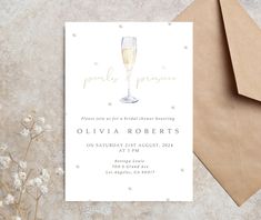 a white card with a champagne glass on it next to some brown envelopes and flowers