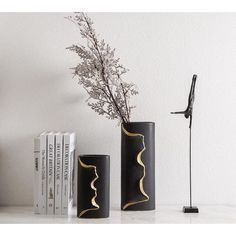 two black vases sitting next to each other on a white table with books and a lamp