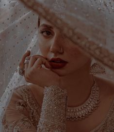 a woman in a white dress and veil with her hand on her chin looking at the camera