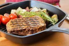 steak, potatoes and tomatoes in a skillet on a wooden table with utensils