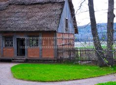 an old house with a thatched roof next to a tree and grass area in front of it