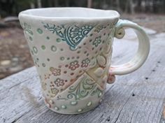 a ceramic coffee cup sitting on top of a wooden table next to trees and bushes