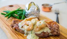 a wooden cutting board topped with meat covered in gravy next to green beans