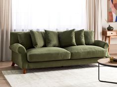 a green couch sitting in front of a window next to a table with a vase on it