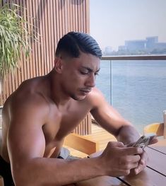 a shirtless man sitting at a table looking at his cell phone