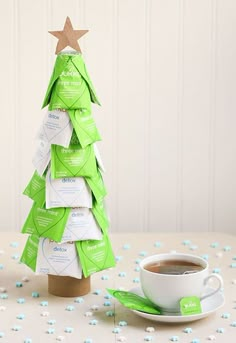 a cup of coffee sitting next to a small christmas tree made out of tea bags