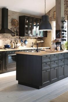 a kitchen with black cabinets and an island in the middle is shown, surrounded by brick walls