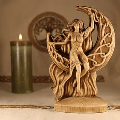 a wooden sculpture of a woman on the moon next to a lit candle