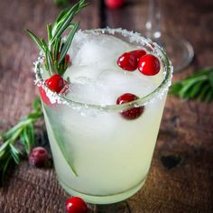 a cocktail with cranberries and rosemary garnish sits on a wooden table