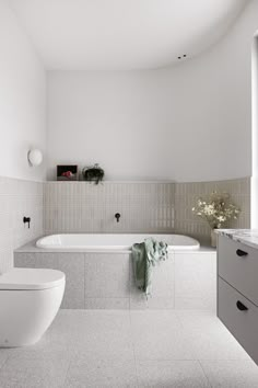 a white bathroom with two toilets and a bathtub next to each other in front of a window