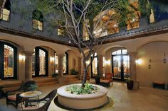 an indoor courtyard with chairs, tables and a tree in the center is lit up at night