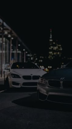 two cars parked in front of a tall building at night with the city lights behind them