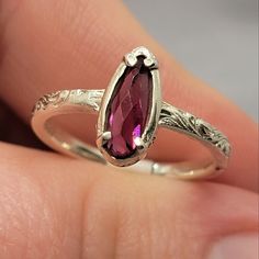 a woman's hand is holding a ring with a large purple stone in it