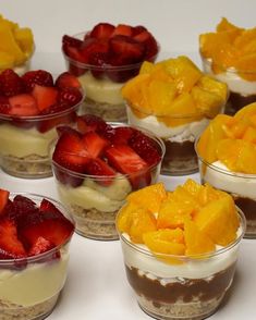 several desserts are arranged in small bowls on a white counter top, with fruit toppings