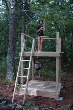 a woman standing on top of a wooden platform in the woods next to a tree