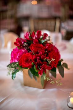 a vase filled with red flowers sitting on top of a white tablecloth covered table