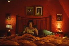 a woman sitting on top of a bed in a room with red walls and paintings