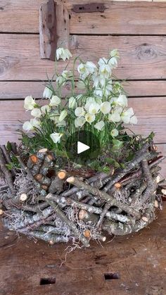 a flower arrangement made out of branches and twigs with white flowers in the center on a wooden table