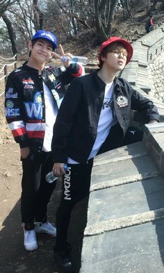 two young men standing next to each other in front of stone steps with trees behind them