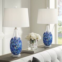 two blue vases with white flowers sit on a table in front of a couch