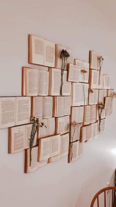 several open books are hung on the wall with flower stems attached to them, along with two wooden chairs