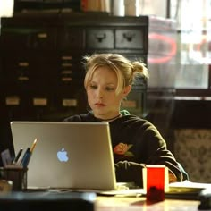 a woman sitting at a table with a laptop computer in front of her and an apple logo on the screen