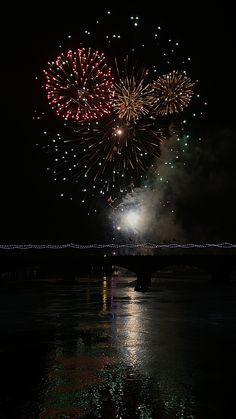 fireworks are lit up in the night sky over water with reflections on the water surface