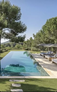 an outdoor swimming pool with lounge chairs and umbrellas in the grass next to it