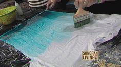 a woman is using a brush to paint a piece of cloth on the floor with blue and green dye