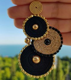 a pair of black and gold beaded earrings with pearls hanging from it's sides