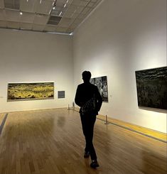 a person walking in an art gallery looking at paintings on the wall and wood floor