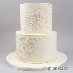 a three layer white wedding cake with intricate lace on the top and bottom tiers