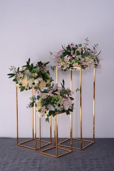 three gold geometric plant stands with flowers on each side and greenery in the middle