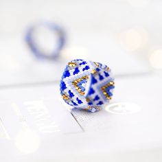 a blue and white beaded ring sitting on top of a piece of paper with gold accents