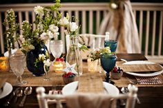 the table is set with white and blue flowers in vases, plates and silverware