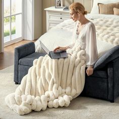 a woman sitting on top of a bed with a blanket over her head and holding a laptop