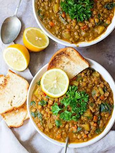 two bowls of lentula soup with bread and lemon slices on the side, one being held by a hand