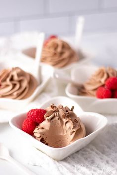 three small white bowls filled with chocolate ice cream and raspberries on a table