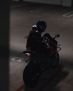 a man riding on the back of a red motorcycle in parking lot at night time