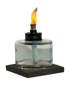 a small glass jar with a lit candle in it on a wooden stand against a white background