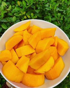 a white bowl filled with cut up mangoes on top of a green leafy field