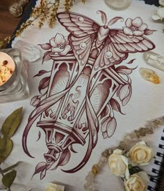 a drawing on paper with flowers and candles next to it, including an ink pen