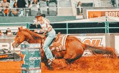 a woman riding on the back of a brown horse next to a barrel in an arena