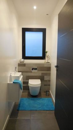 a bathroom with a toilet, sink and mirror on the wall next to a blue rug