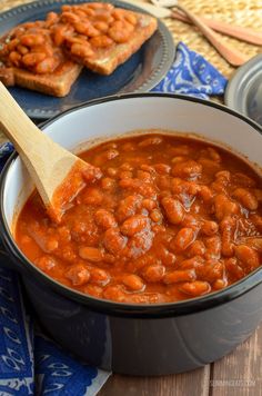 baked beans are in a pot with a wooden spoon next to toast on the table