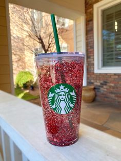 a starbucks cup with red glitter and a green straw on the outside of a house