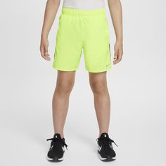 a young boy wearing neon green shorts and black shoes, standing in front of a white background